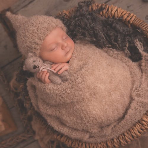 Baby schläft in einer Schale zugedeckt mit einem Tuch, die Schale steht auf einer alten Holztür