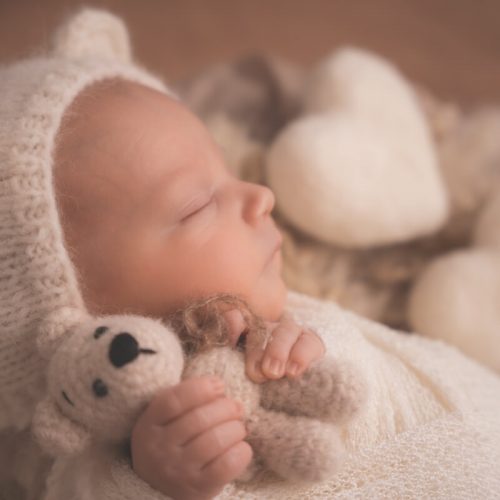 Baby Junge mit Herz im Hintergrund und kleinen Strickbären in der Hand