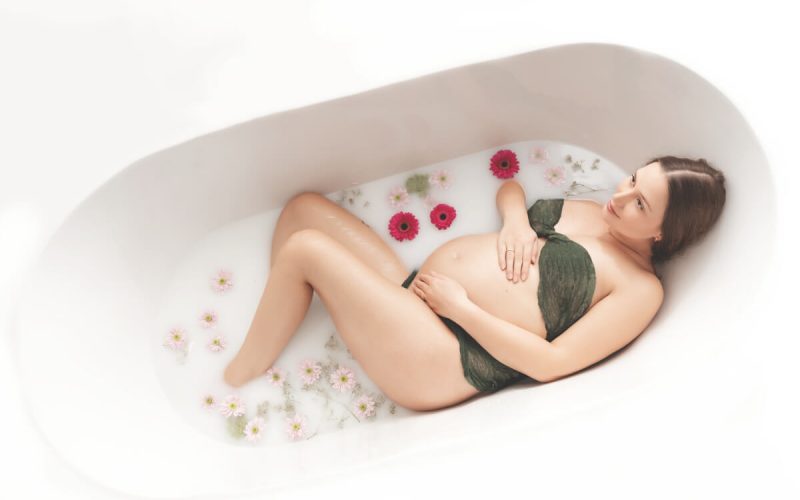 Schwangere mit schwimmenden Blumen in der Badewanne