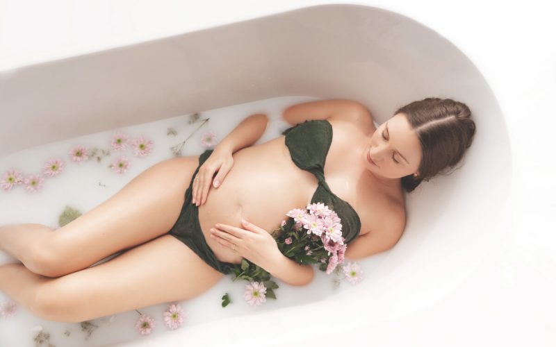 Schwangere mit Blumenstrauss in Badewanne